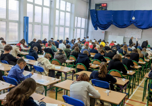 Uczniowie biorący udział w konkursie siedzą w ławkach w sali gimnastycznej.