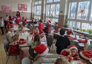 Stołowka wypełniona uczniami jedzącymi obiad w czapkach Mikołaja.